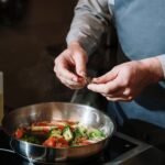 Kucharz doprawia na patelni warzywny stir fry świeżymi ziołami