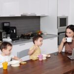 Mama z dwoma synami jedzą śniadanie przy laptopie w kuchni