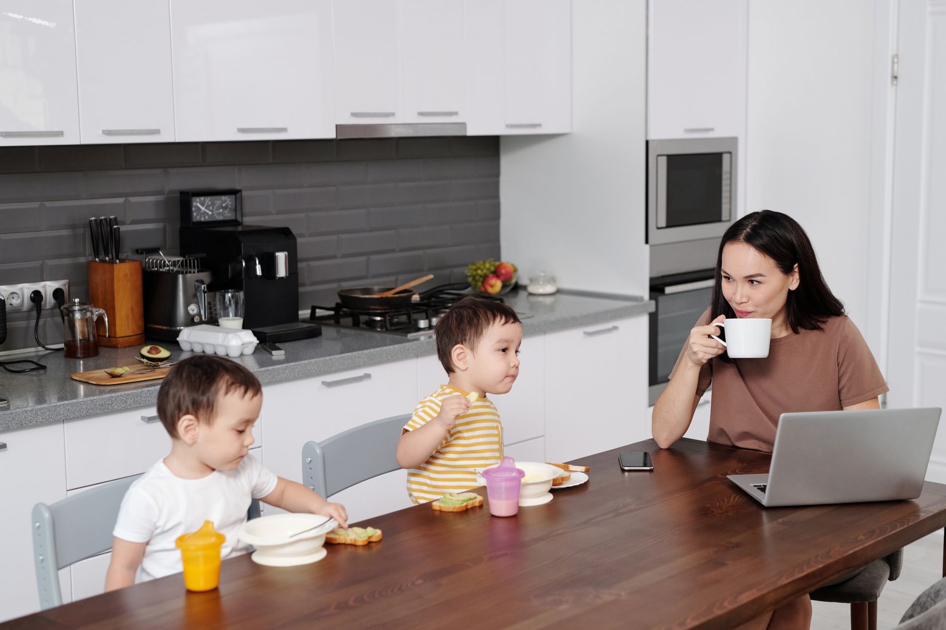 Mama z dwoma synami jedzą śniadanie przy laptopie w kuchni